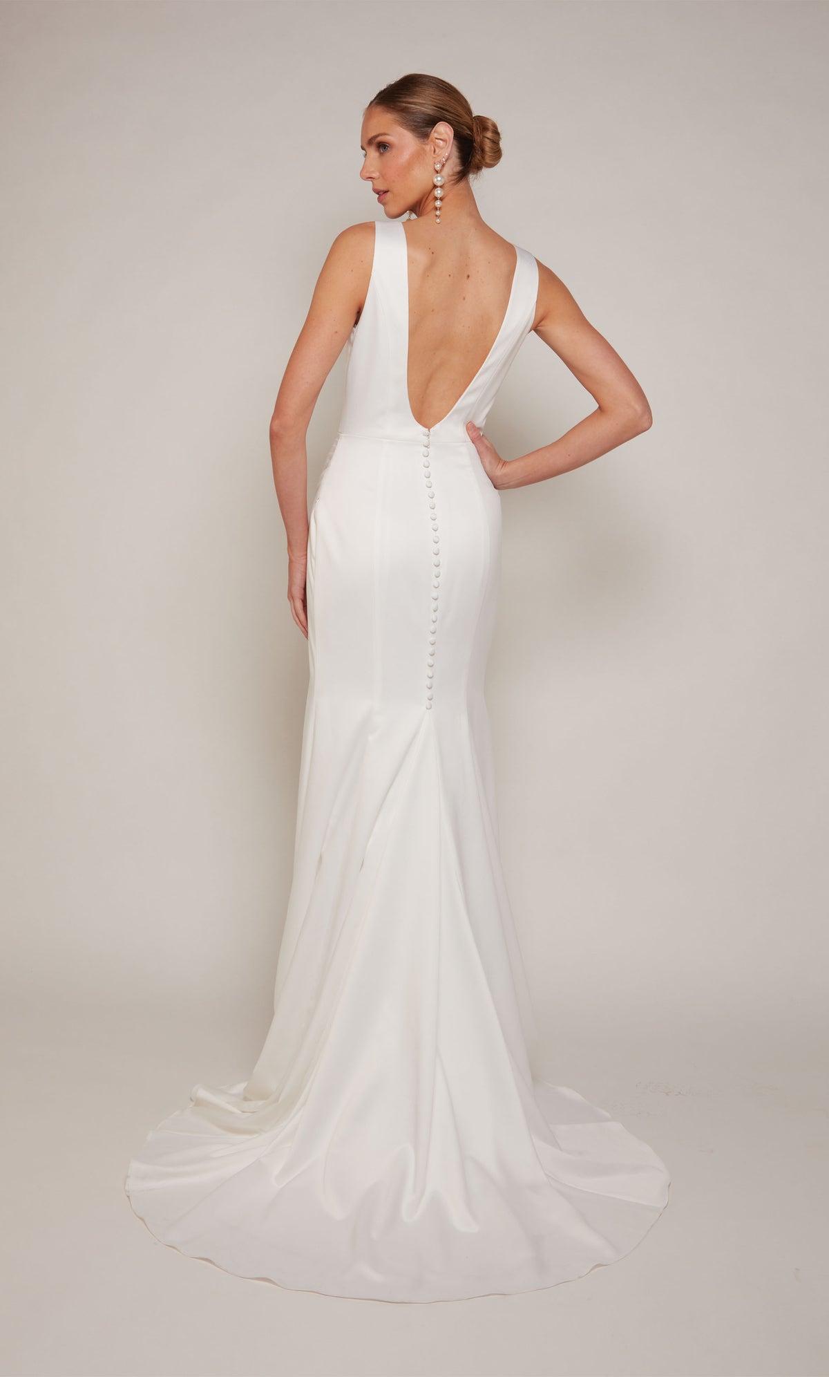A white, satin wedding gown highlighting a V-shaped open back and train adorned with satin covered buttons.