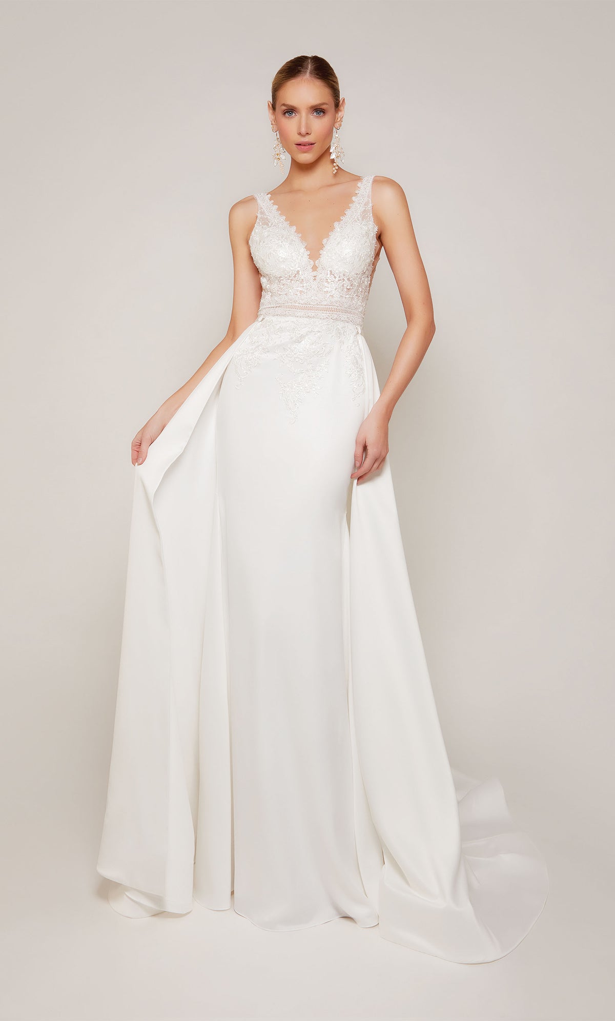 Luxurious satin sheath wedding dress in white with a V-neckline and delicate lace details. The dress comes with a detachable train that adds a hint of drama and formality during the ceremony, and can be detached for a more understated reception style.