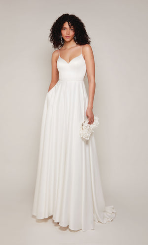 A classic, satin A-line wedding dress featuring a semi-sweetheart neckline and pearl embellishments on the straps, at the waistline, and on the illusion back. The dress also has an elegant train with satin-covered buttons down the back.
