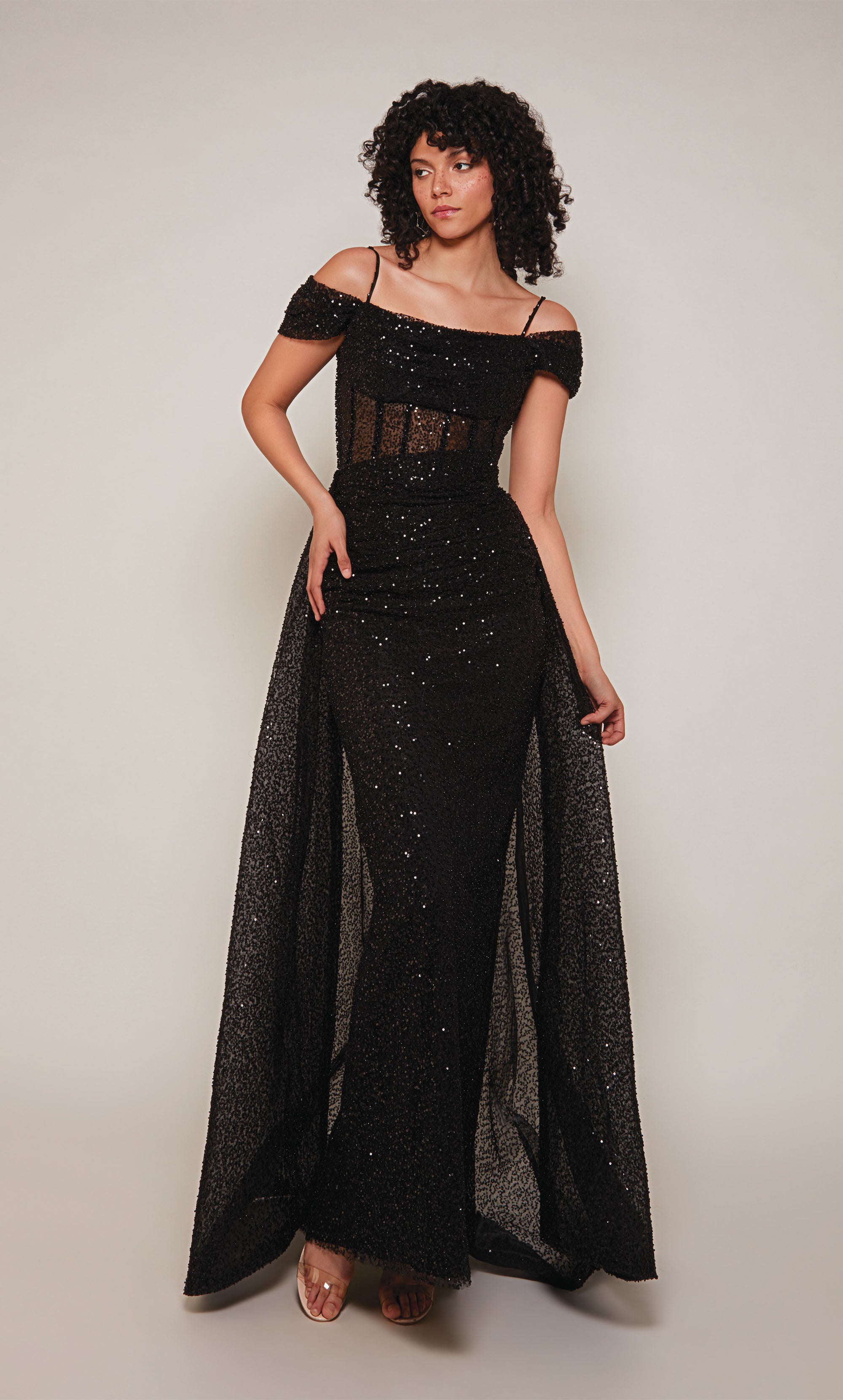 A chic, black corset wedding dress in beaded tulle. The highlights of the dress are an off-the-shoulder neckline with thin spaghetti straps, a sheer bodice, and a fitted skirt. The overskirt adds the perfect amount of sophisticated drama.
